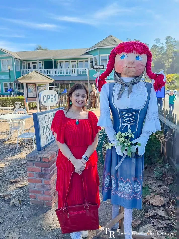 Visitor in a red dress posing with a red-haired scarecrow in a blue dirndl in Cambria