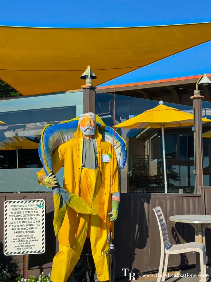 Fisherman scarecrow in a yellow rain slicker holding a big fish on a Cambria patio