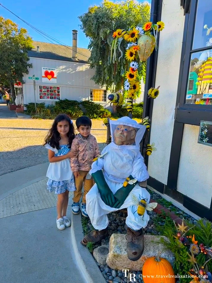Kids posing with a sunflower-trimmed scarecrow on a street in Cambria