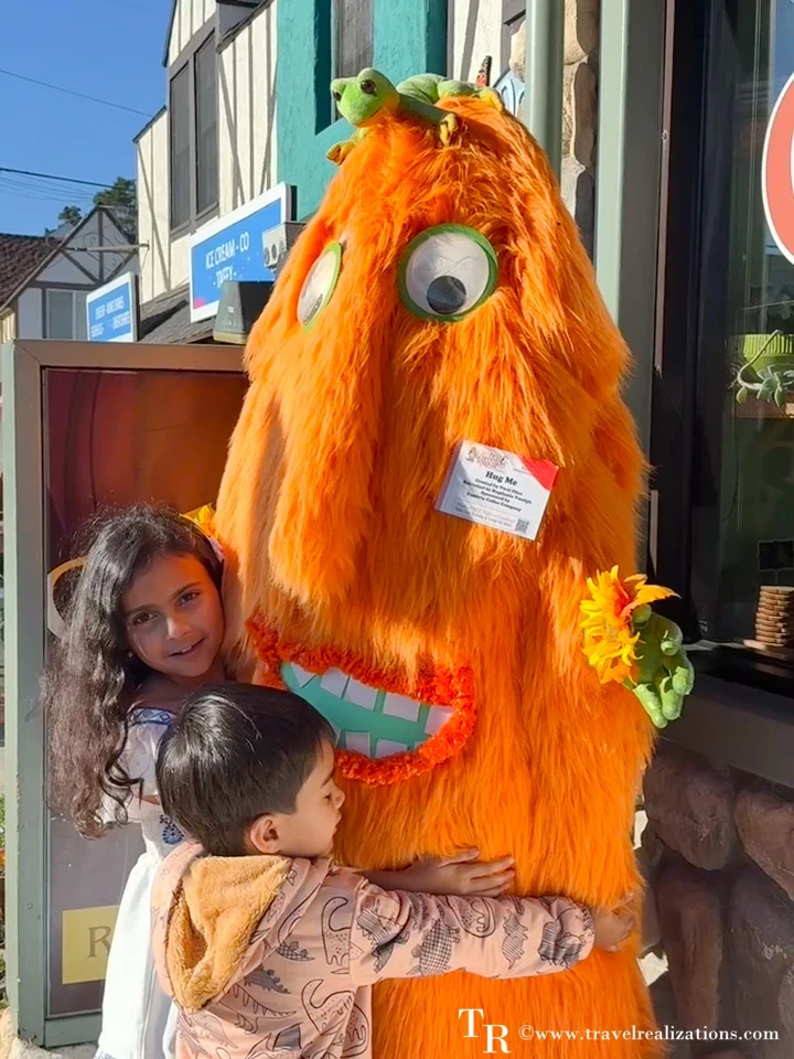Kids hugging a fluffy orange monster scarecrow in Cambria