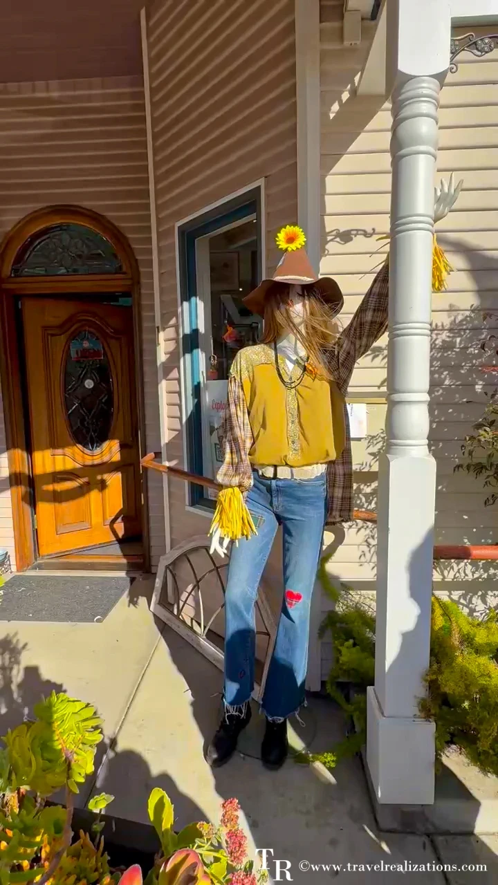 Cowgirl scarecrow in a yellow vest and jeans on a porch in Cambria