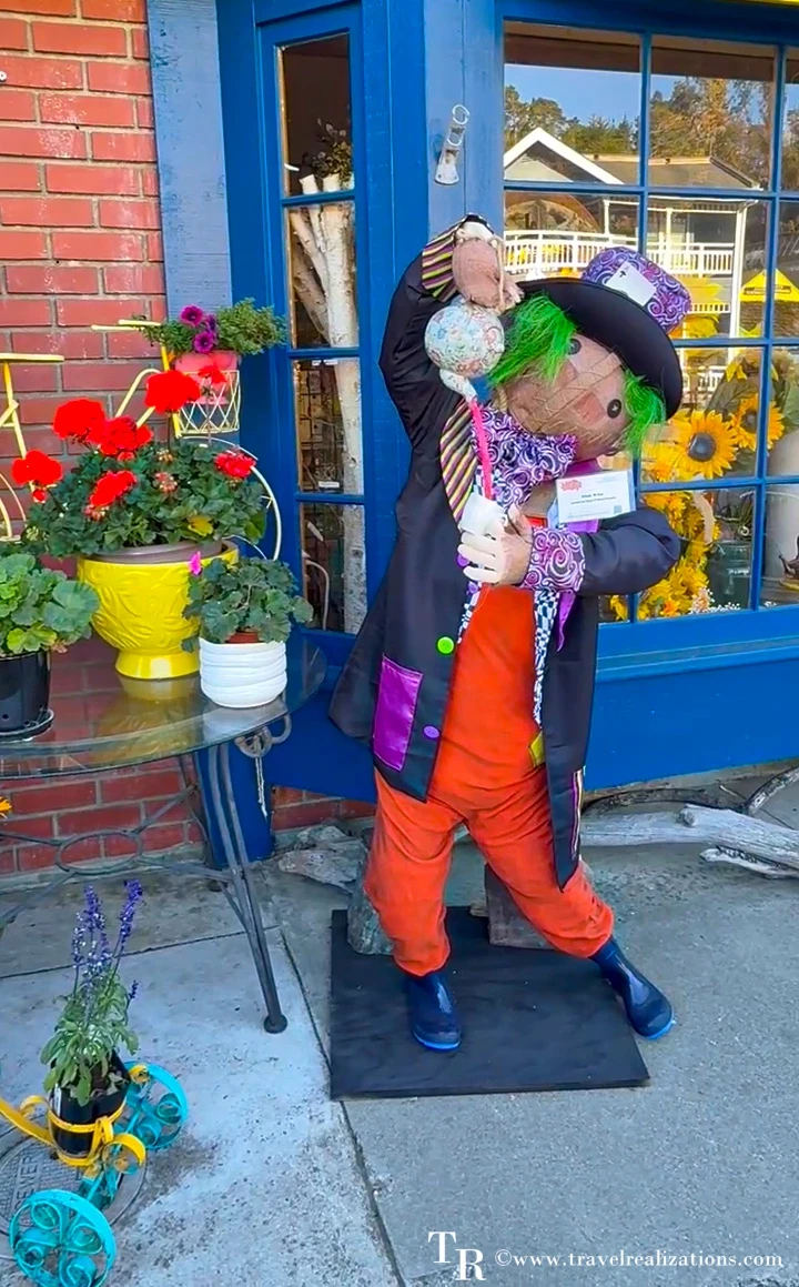 Mad Hatter scarecrow with a green wig and top hat outside a blue shop door in Cambria